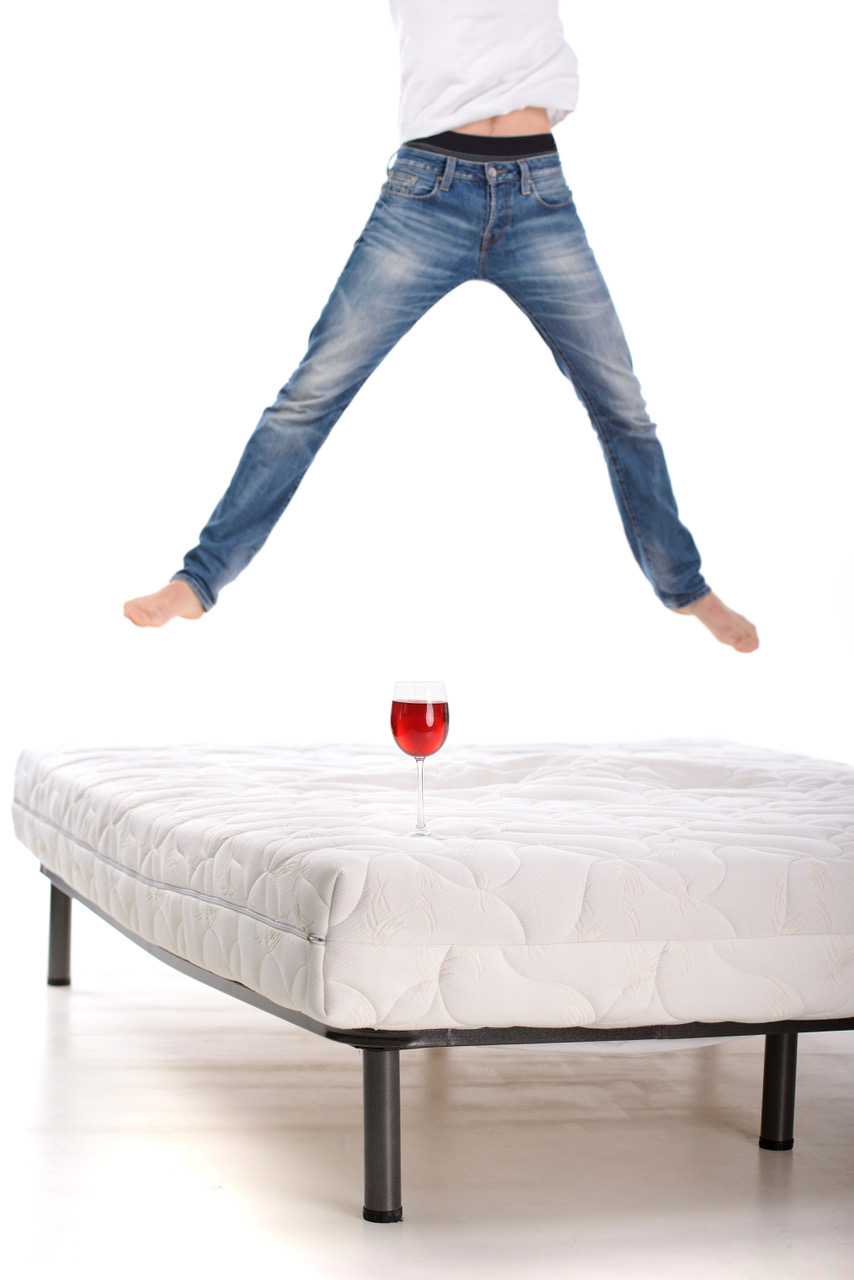 Muž skáče po matraci a sklenička vína je položená na matraci